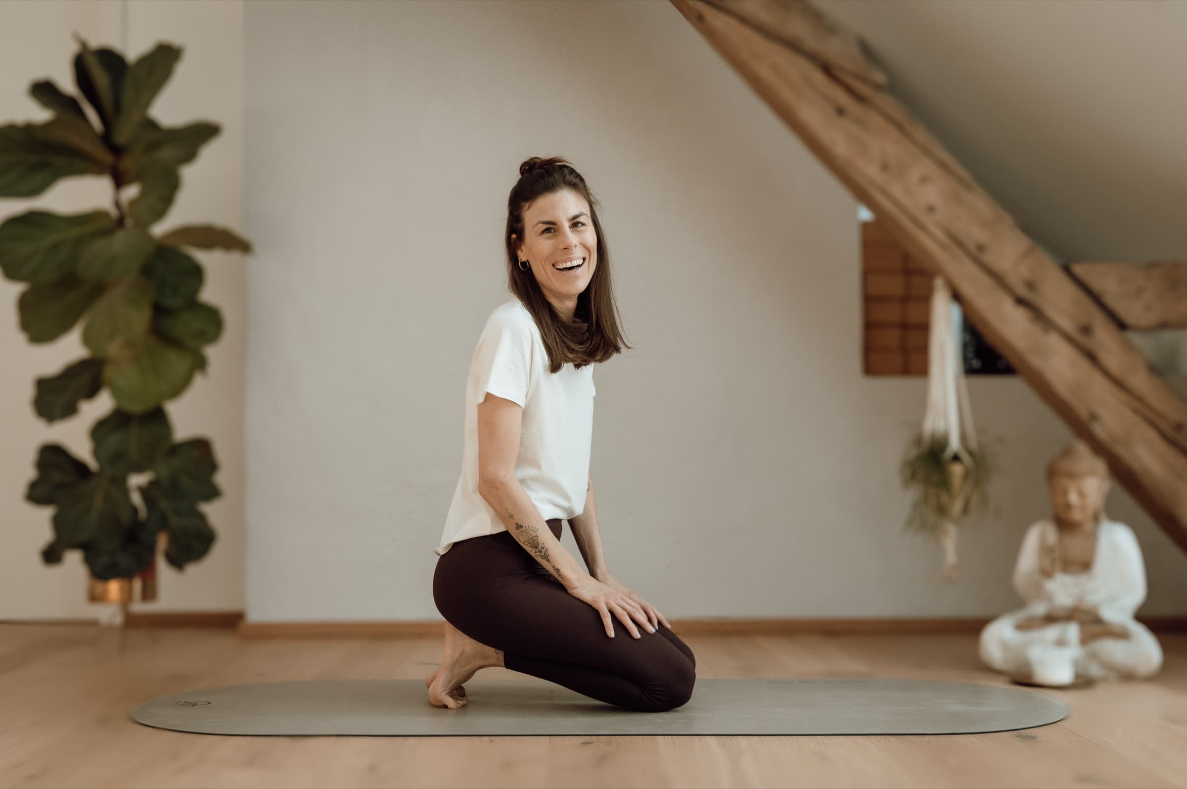Lisa kniend auf der Yogamatte, lachend, im Studio mit Buddha-Figur